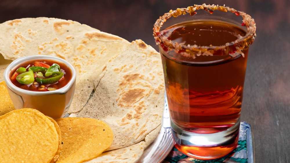 Indulge in the perfect chinguirito pairing - a sip of aguardiente accompanied by warm tortillas and salsa.