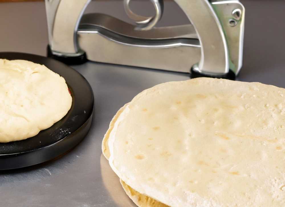 A tortilla press and a bowl of dough used to make homemade tortillas.