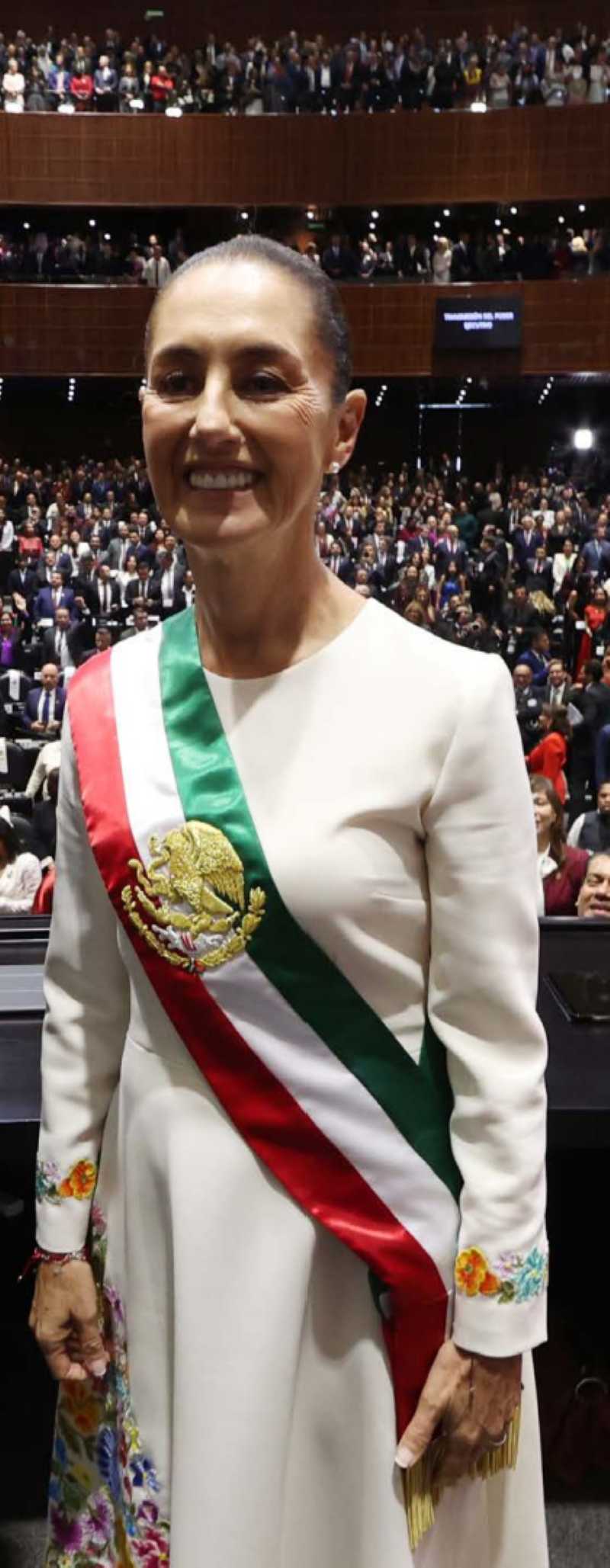 Mexico's new president stands at a podium during her inauguration ceremony, addressing a large crowd.