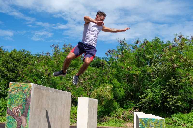 Young person doing a parkour move in a garden with eco-bricks and plants in the background.