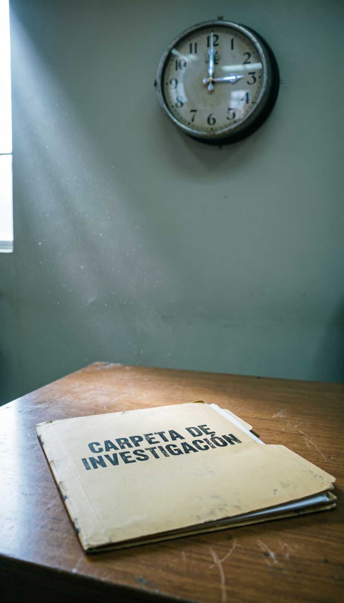 A manila folder labeled CARPETA DE INVESTIGACIÓN sitting on an empty wooden desk.