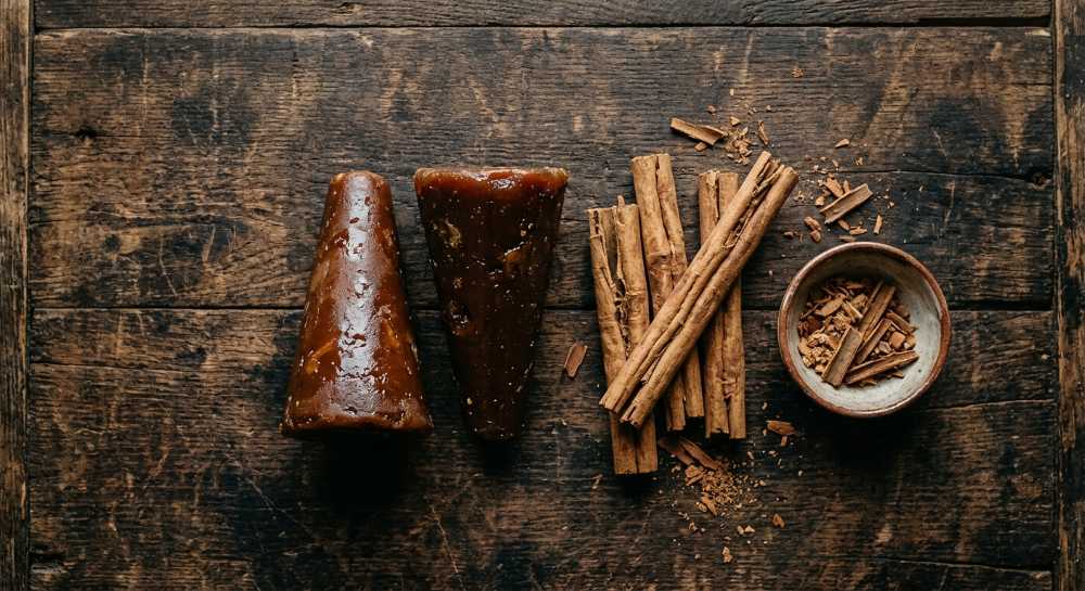 Two dark brown cones of piloncillo sugar placed next to a Mexican cinnamon sticks.