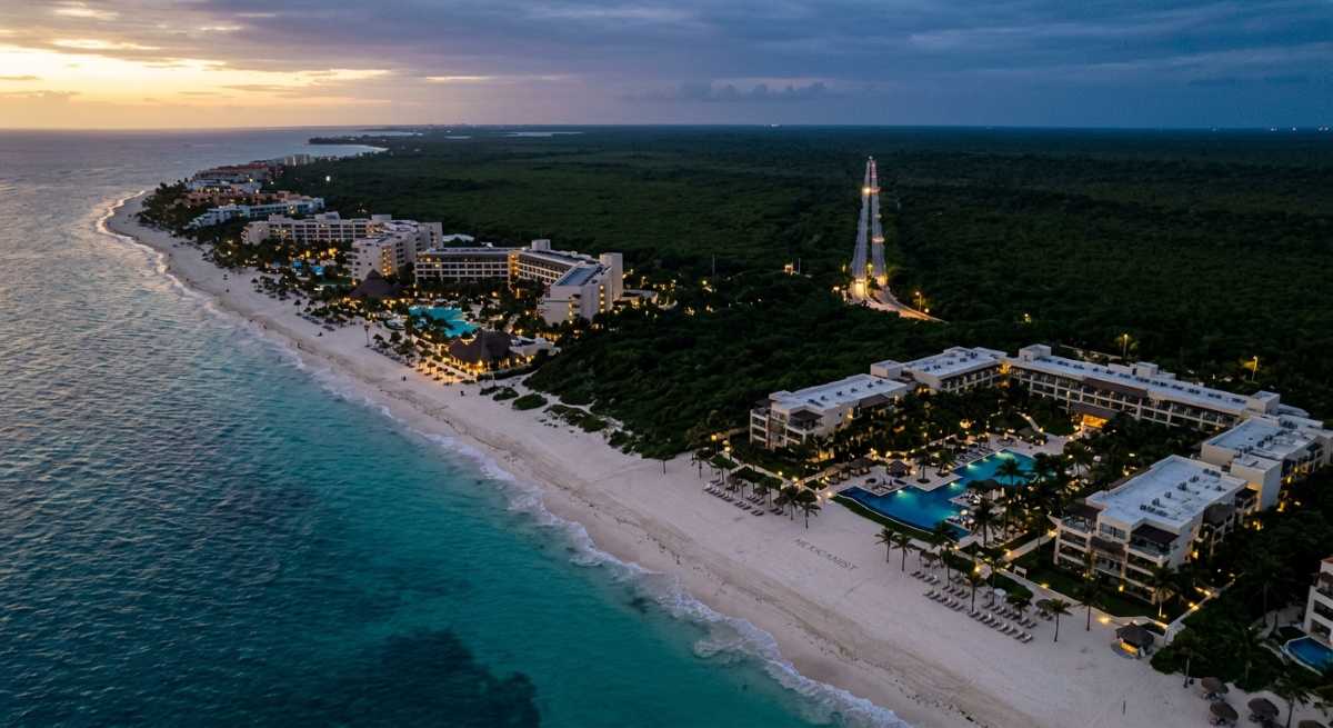 Aerial view of the Riviera Maya coastline at dusk showing resort hotels along a pristine Caribbean beach.