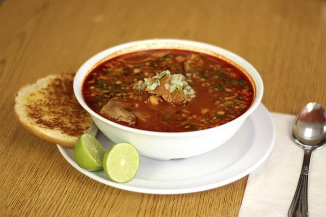 Steaming hot bowls of red pozole, topped with crunchy radishes, fresh lettuce, and creamy avocado.