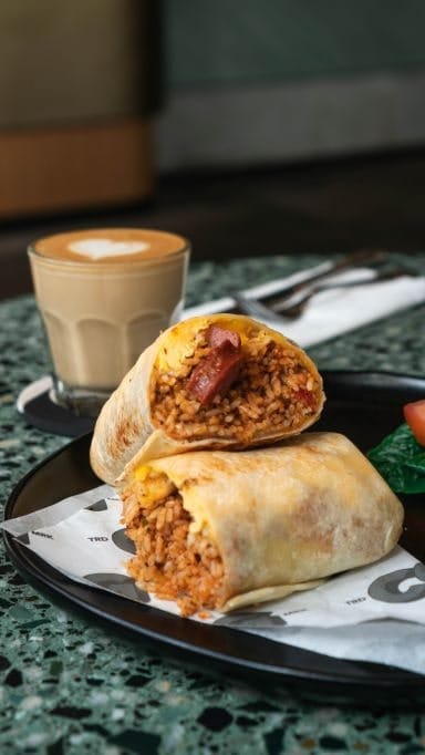 A glass of coffee with milk and Mexican burrito served on the black plate.