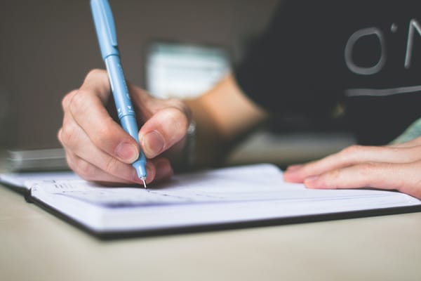 Person holding blue ballpoint pen writing in notebook.