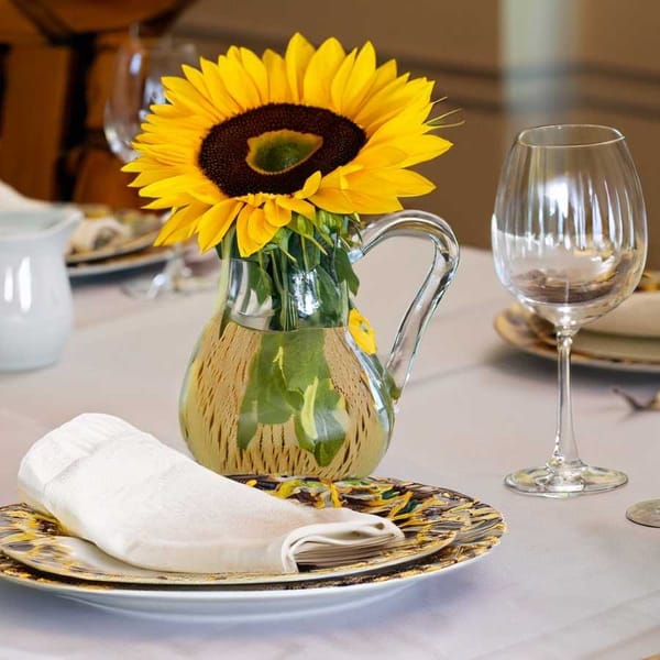 A well-set table adorned with a small pitcher, a sunflower, and an embroidered napkin.