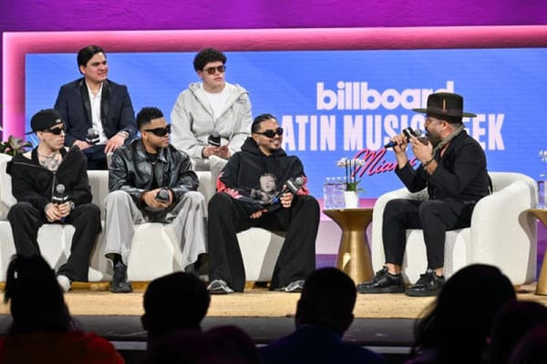 A group of Latin music artists sitting on a stage, discussing their music and experiences.