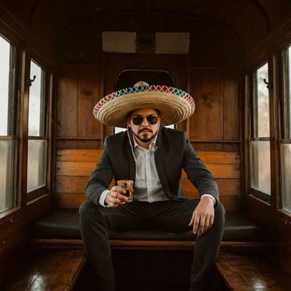 A man in a sombrero drinking tequila on a train in Mexico.