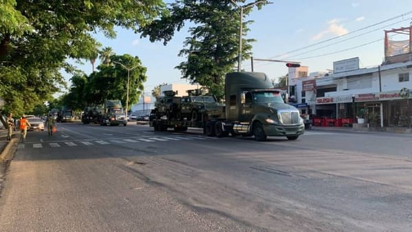 A military convoy of armored vehicles driving through a rural Mexican town.