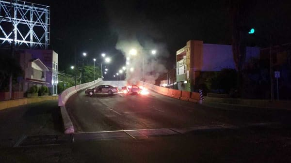 A burning car in the middle of a Culiacán street at night, with smoke billowing into the air.