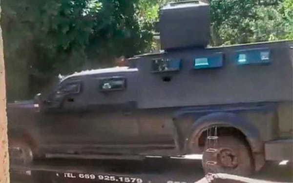 Heavily armored green pickup truck with extended cabin and rotating turret, being loaded onto a flatbed truck.