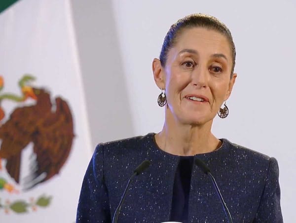 President Claudia Sheinbaum speaking at a podium, with a serious expression, and a background of a Mexican flag.