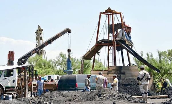 Rescue workers in hard hats and safety gear standing at the entrance of a coal mine.