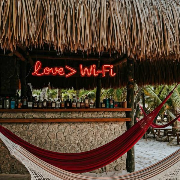 A neon sign reading "Love > Wi-Fi" hangs above a palm-thatched beach bar in Tulum.