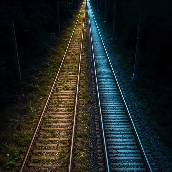 A faded, overgrown railroad track slowly transforming into a modern, brightly lit one.