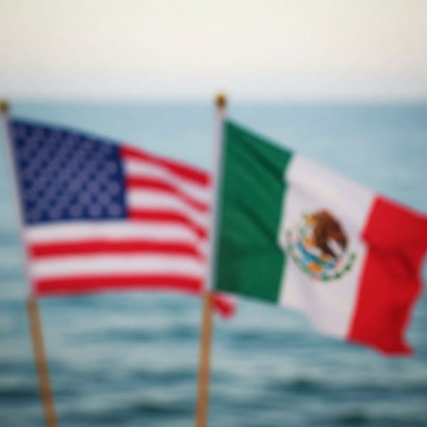 Blurred image of American and Mexican flags juxtaposed against an ocean background.