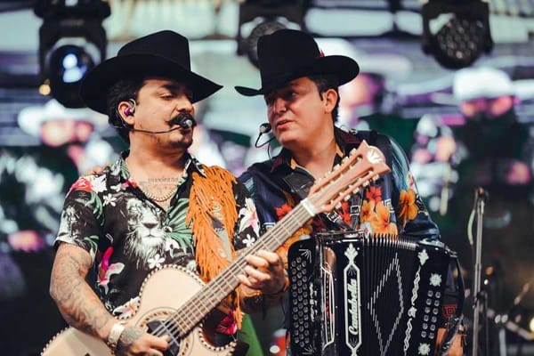 An image featuring members of a musical group Los Dos Carnales, performing  on a stage.