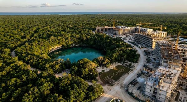Aerial view of a cenote in the Yucatan jungle with construction cranes from hotel developments visible at the edges of the forest.